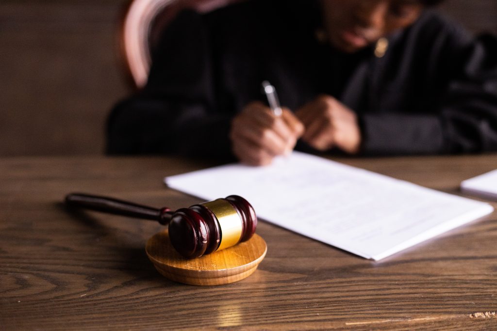 A wooden gavel with a person writing on a document in the background. 